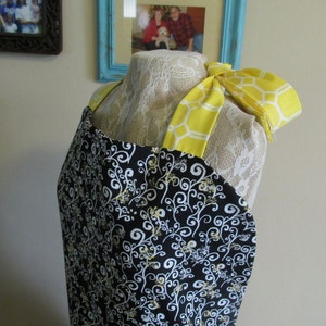 May include: A black and white apron with a yellow and white honeycomb pattern on the straps. The apron has a white and black floral design.