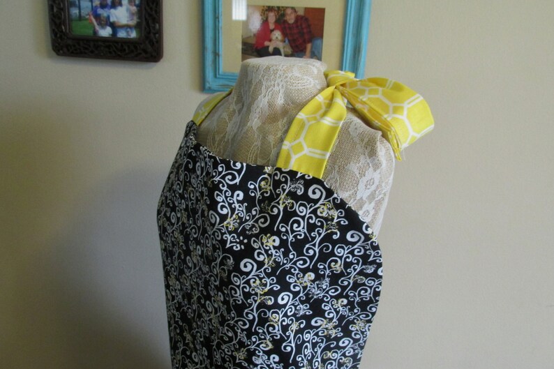 May include: A black and white apron with a yellow and white honeycomb pattern on the straps. The apron has a white and black floral design.