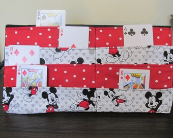 Può includere: Un organizzatore in tessuto rosso e bianco con personaggi di Topolino e pois. L'organizzatore ha sei tasche per contenere le carte da gioco. Le carte nelle tasche sono l'8 di quadri, il jack di quadri, l'asso di quadri, il re di quadri, il 4 di fiori e il re di cuori.