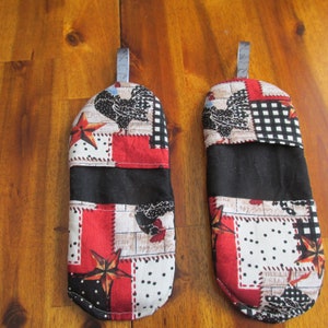 May include: Two red, black, white and blue quilted oven gloves with a rooster and star design. The gloves have a loop for hanging.