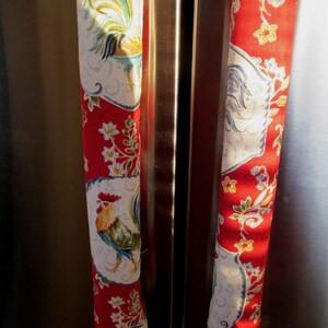 May include: Two red fabric refrigerator door handles with a rooster and floral pattern.
