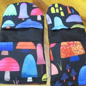 May include: A pair of black oven mitts with a colourful mushroom pattern. The mitts are made of fabric and have a black lining.