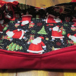 May include: Red fabric Christmas gift basket with a black and white Santa Claus print lining. The print features Santa Claus, Christmas trees, presents, and snowflakes.