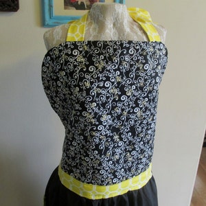 May include: Black and white patterned apron with yellow straps and a yellow trim around the bottom.