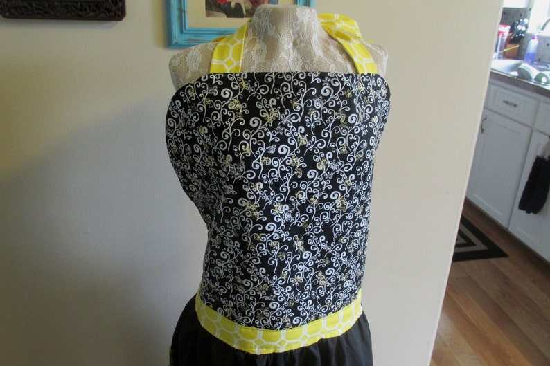 May include: Black and white patterned apron with yellow straps and a yellow trim around the bottom.