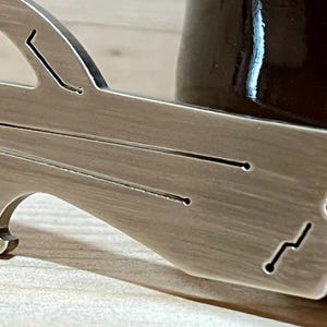 May include: A silver bottle opener with a unique design featuring a curved handle and a bottle opener on the bottom. The opener has a brushed metal finish.