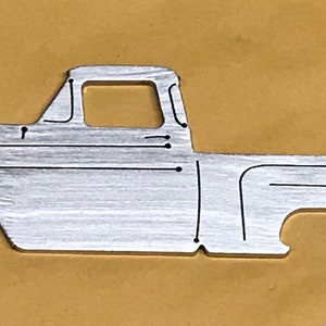 Puede incluir: Un recorte de metal plateado de una camioneta vintage. La camioneta está en vista de perfil y tiene un diseño detallado.