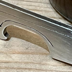 May include: A silver bottle opener with a curved opening for prying off bottle caps. The opener has a smooth, brushed finish.