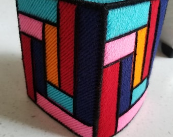 May include: A colorful tissue box cover with a geometric design. The cover is made of fabric and features a variety of colors, including red, blue, orange, pink, and turquoise.
