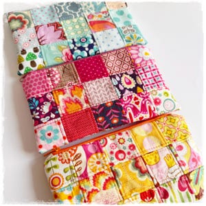 Könnte beinhalten: Drei bunte Patchwork-Stoffbeutel mit Reißverschlüssen. Jeder Beutel besteht aus kleinen, quadratischen Stoffstücken in verschiedenen Mustern und Farben, darunter Blumenmuster, Tupfen und geometrische Designs. Die Beutel sind leicht überlappend angeordnet.