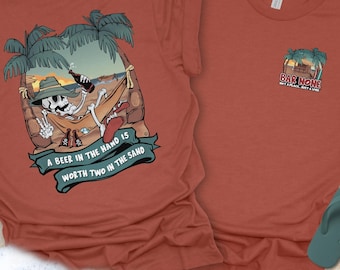May include: Two rust-coloured t-shirts. One features a skeleton in a hammock with the text "A beer in the hand is worth two in the sand." The other has a small logo that says "Bar Home" with a beach scene.