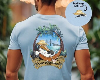 May include: Light blue t-shirt with a cartoon pelican wearing a straw hat and relaxing in a hammock. The graphic includes palm trees, a bridge, and the text "SAINT PETERSBURG FLORIDA".