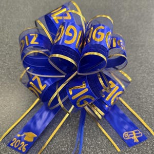 May include: A blue and gold graduation bow with the year "2026" printed on the ribbon. The bow is made of a sheer blue material with gold trim and the year "2026" printed in gold. The bow is a decorative item for graduation celebrations.