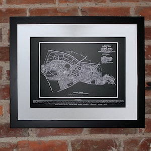 May include: A black framed print of a vintage map of a town with the text "Old Town" in the bottom center. The print is hanging on a brick wall with a decorative hook and a patterned fabric hanging from it. Three green and yellow duck figurines are on a white shelf below the print.