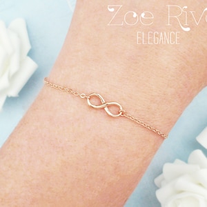 May include: A delicate gold bracelet with an infinity symbol at its centre. The bracelet is attached to a fine chain. The image also includes the text "Zoe River Elegance".