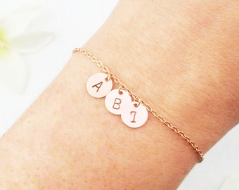 May include: A delicate rose gold bracelet featuring three small, circular charms engraved with the letters "A", "B", and the number "1". The bracelet has a chain design. The text "Zoe River Elegance" is visible in the background.