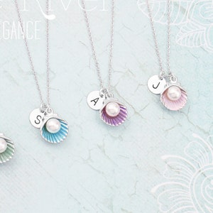 May include: Four silver necklaces with seashell pendants. Each pendant is a different colour: green, blue, purple, and pink. Each seashell holds a white pearl and a small silver initial charm. The text "Zoe River Elegance" is in the background.