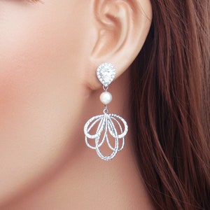 May include: Silver drop earrings with a clear, pear-shaped stone at the top, a small pearl, and an openwork design. The earrings are designed to dangle, creating a delicate and elegant look. These earrings are suitable for special occasions and formal events.