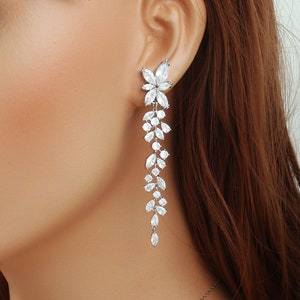 May include: Elegant silver-toned drop earrings featuring a floral design at the earlobe, cascading into a series of marquise and pear-shaped crystals. The earrings are designed to dangle and catch the light, adding a touch of sparkle. The earrings are a part of the Zoe River Elegance collection.