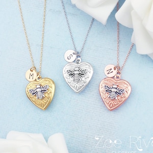 May include: Three heart-shaped lockets with bee and initial charms. The lockets are gold, silver, and rose gold, each with a delicate chain. The bee design is centered on the locket, and each locket has a different initial charm.