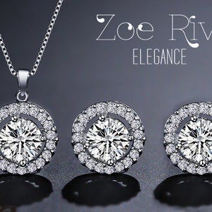 May include: A silver necklace and matching earrings set. The pendant and earrings feature a large, round, clear gemstone surrounded by a halo of smaller, sparkling stones. The set is displayed on a dark background, with the text "Zoe River ELEGANCE".