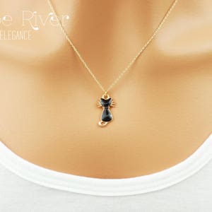 May include: A gold-colored necklace with a black cat pendant. The pendant is a stylized cat silhouette with a detailed face and tail. The necklace is displayed against a white background, with the text "Zoe River Elegance" in the upper left corner.