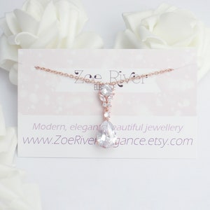 May include: A rose gold necklace with a large, pear-shaped clear crystal pendant. The pendant is suspended from a delicate chain and is accompanied by smaller, clear crystals. The necklace is displayed on a card with the text "Modern, elegant beautiful jewellery".