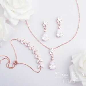 May include: A rose gold jewelry set featuring a bracelet, necklace, and earrings. The bracelet and earrings have a leaf design, while the necklace and earrings have a teardrop-shaped pendant. The jewelry is adorned with clear crystals.