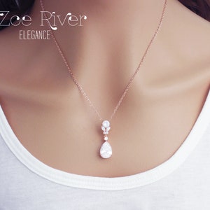 May include: Rose gold necklace with a pendant featuring a pear-shaped clear gemstone. The pendant is suspended from a delicate chain. The text "Zoe River Elegance" is visible in the upper left corner.