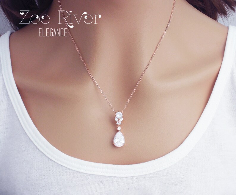 May include: Rose gold necklace with a pendant featuring a pear-shaped clear gemstone. The pendant is suspended from a delicate chain. The text "Zoe River Elegance" is visible in the upper left corner.
