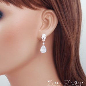 May include: Elegant silver-toned drop earrings with sparkling clear crystals. The earrings feature a round stud, a floral design, and a large pear-shaped crystal. The earrings are from the Zoe River Elegance collection.