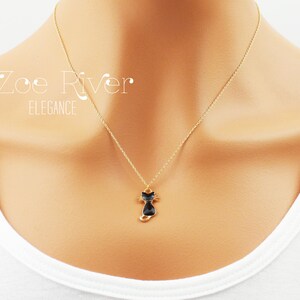 May include: A gold-colored necklace with a small black cat pendant. The cat pendant has a gold outline and is suspended from a delicate chain. The text "Zoe River Elegance" is visible in the upper left corner.