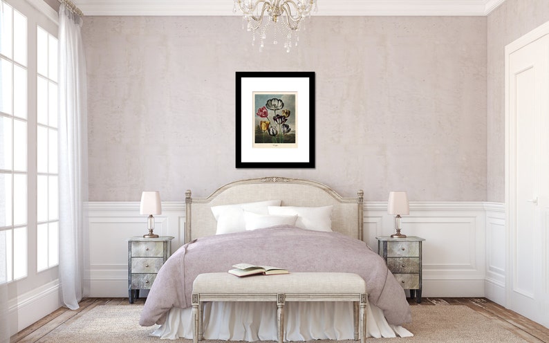 May include: A framed botanical print featuring colorful flowers, displayed above a bed in a bedroom setting. The print has a black frame and is mounted on a white mat. The bedroom has a neutral color palette with a bed, nightstands, and a bench.