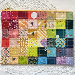May include: A rectangular zipped pouch constructed from a grid of multicoloured fabric squares. The patchwork design features various patterns including floral, geometric, and animal motifs in shades of red, orange, yellow, green, blue, and purple.