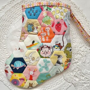 May include: A patchwork stocking featuring hexagonal fabric pieces with illustrated designs of animals and food. The stocking has a patterned trim and a loop for hanging. The overall design is bright and cheerful, with a variety of colours.