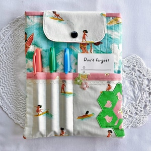 May include: A fabric organizer with a tropical surf theme. The organizer features a flap with a black button, pockets, and a note that says "Don't forget!". It has a pink and white striped pattern with images of surfers and waves.
