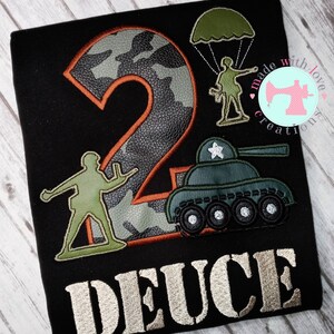 May include: A black t-shirt with a camouflage number two, a green toy soldier, a green toy tank, and the word "DEUCE" in a silver font.