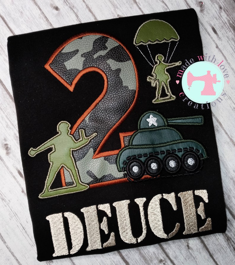 May include: A black t-shirt with a camouflage number two, a green toy soldier, a green toy tank, and the word "DEUCE" in a silver font.