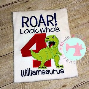 May include: White t-shirt with a green dinosaur and red number 4. The text "Roar! Look Who's Williamsaurus" is embroidered on the shirt.