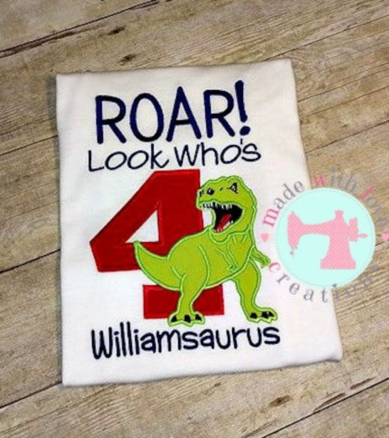 May include: White t-shirt with a green dinosaur and red number 4. The text "Roar! Look Who's Williamsaurus" is embroidered on the shirt.