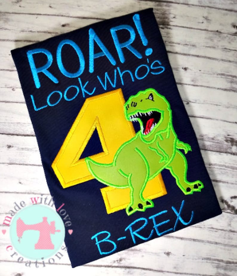 May include: A blue t-shirt with a yellow number four and a green dinosaur with the text "Roar! Look Who's B-Rex" in blue and green.