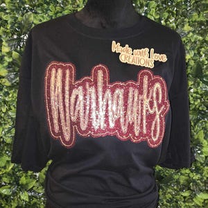 May include: Black t-shirt with a gold and maroon glitter design that says "Warhawks" and a small tag that says "Made with Love Creations".