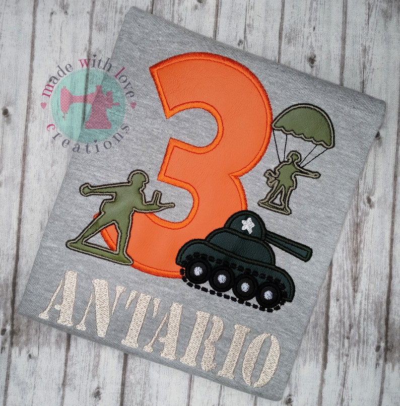 May include: A gray t-shirt with an orange number 3, a green tank, a green soldier with a parachute, and a green soldier holding a gun. The text "ANTARIO" is embroidered in beige below the design.