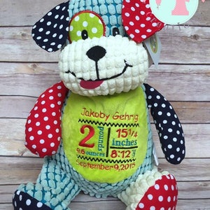 May include: A plush, multi-colored dog toy with a green, white, and black eye, red and white polka dot ears, and red and white polka dot feet. The toy is personalized with the name "Jakoby Gehrig", birth weight of "2 pounds 9.6 ounces", birth length of "15 1/4 inches", and birth date of "September 9, 2015".