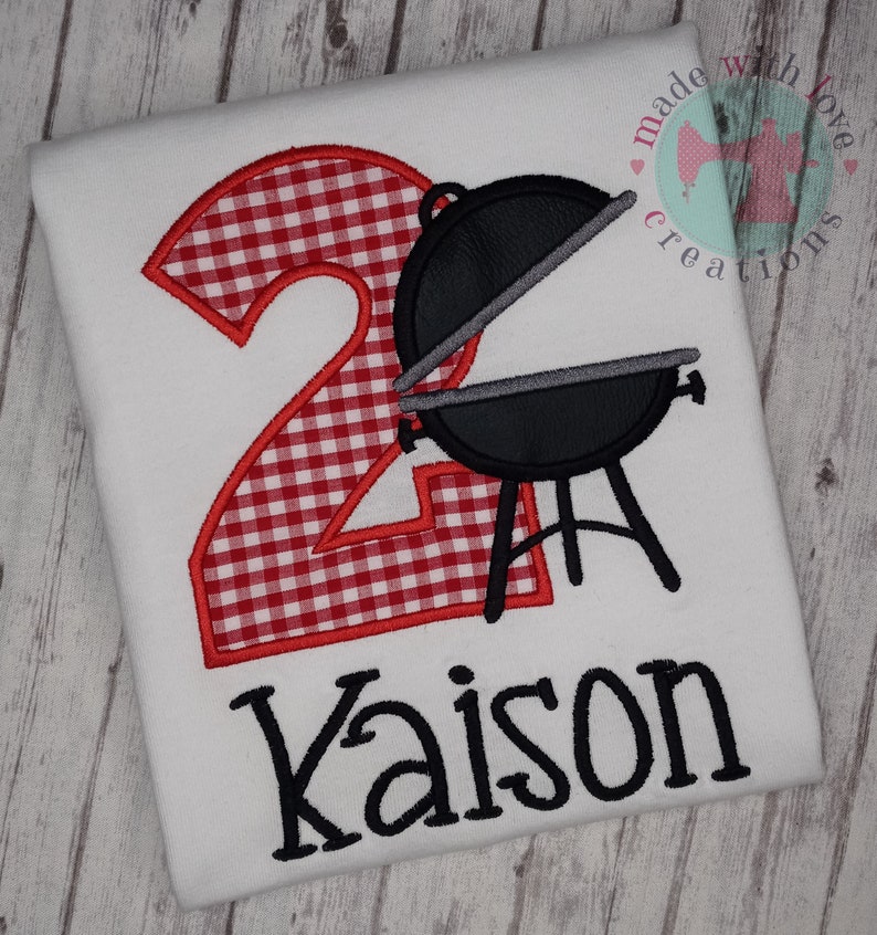 May include: Red and white gingham number two with a black grill and the name Kaison in black embroidery on a white t-shirt.