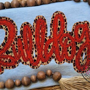 May include: Red and black glitter iron-on patch with the word "Bulldogs" in a cursive font. The patch has a leopard print design.