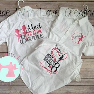 May include: Three white button-down shirts with long sleeves. One shirt features the text "Meet me at the Barre" with pink ballerina silhouettes. Another shirt has a pink circle with a ballerina and the name "Emma". The third shirt displays a heart graphic with the text "My heart beats in 8 counts" and a ballerina silhouette.