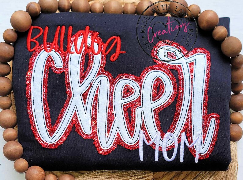 May include: A black t-shirt with red and white sequined lettering that reads "Bulldog Cheer Mom".