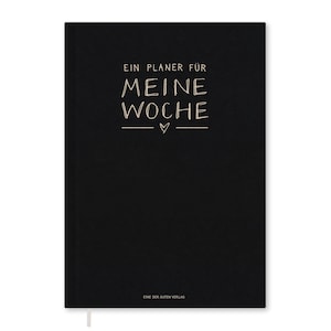 Könnte beinhalten: Ein schwarzer Planer mit dem Text "EIN PLANER FÜR MEINE WOCHE" in handschriftlichem Stil, mit einem kleinen Herzsymbol. Der Planer hat ein weißes Lesebändchen und den Text "EINE DER GUTEN VERLAG" unten.