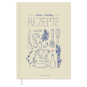 Op de afbeelding: Een beige receptenboek met de tekst "Meine liebsten Rezepte" in blauwe letters. De omslag heeft een blauwe illustratie van verschillende keukengerei en ingrediënten, waaronder een garde, een deegroller, een zeef, een fles olie en een takje lavendel.